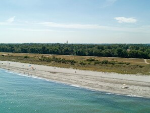 Luchtbeeld van een strand met helderblauw water, een zandstrand en een bebost gebied op de achtergrond.