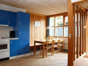 Une cuisine compacte avec des meubles bleus, une cuisinière blanche et un coin repas comprenant une table et des chaises en bois.