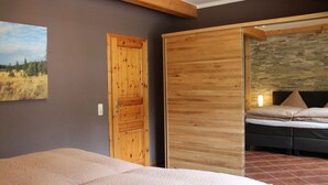 A bedroom with a bed, a wooden wardrobe, a door, and a stone wall. - Holiday Apartment "pohlberg" (Annaberg-Buchholz)