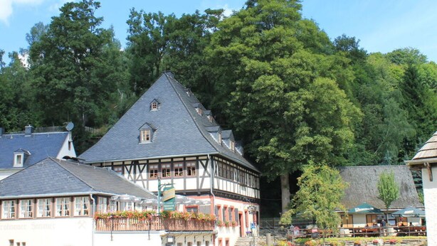 A traditional half-timbered building with a steeply pitched roof, surrounded by lush greenery and a clear sky. - Holiday Apartment "pohlberg" (Annaberg-Buchholz)