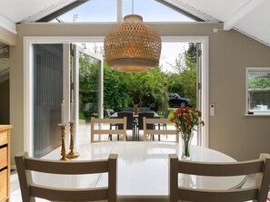 A dining area with a white table and chairs, a hanging light fixture, and a view of the outdoors.