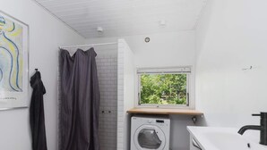 Une petite salle de bain équipée d’un lave-linge, de toilettes et d’une fenêtre donnant sur un espace verdoyant.