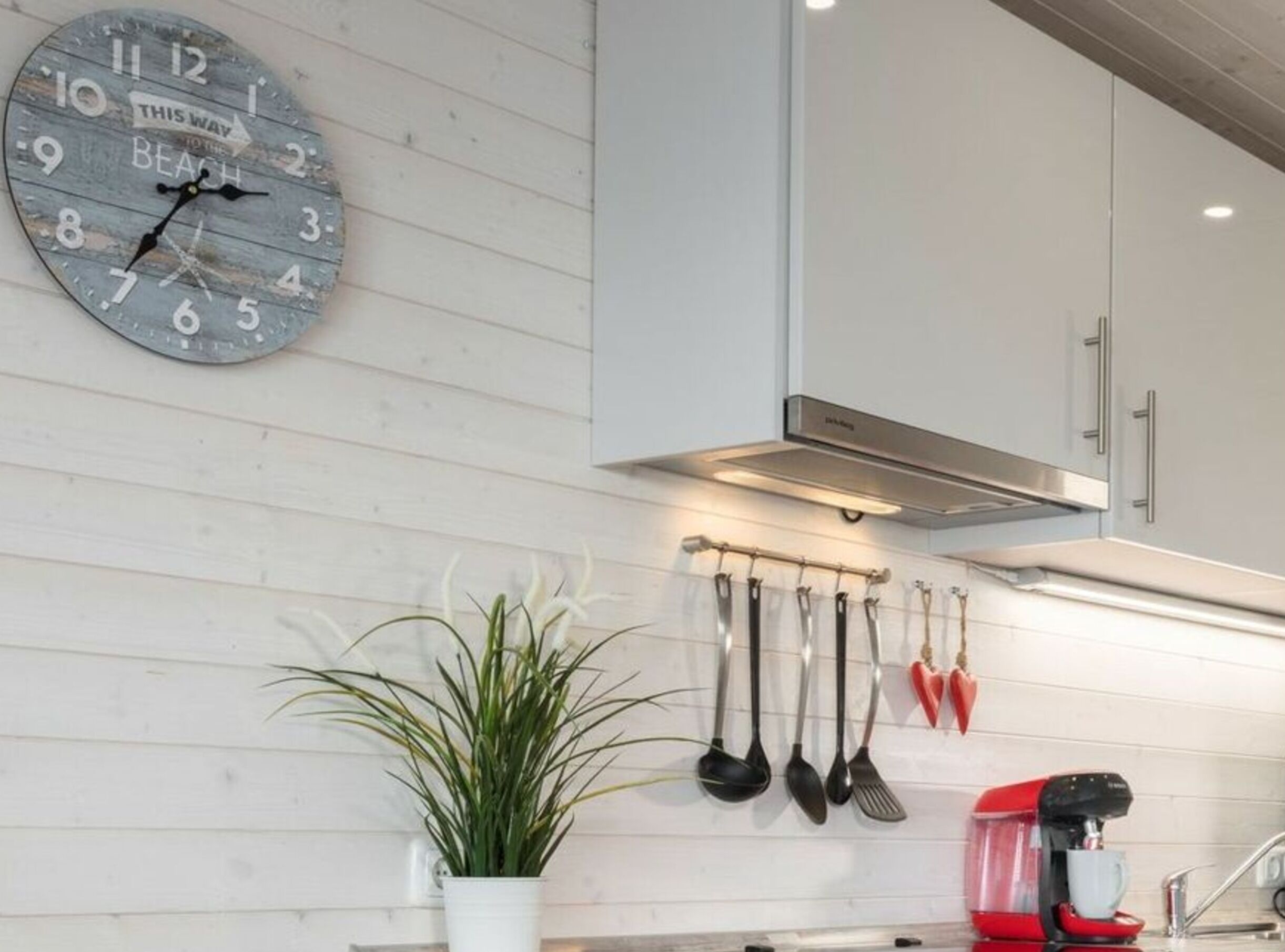 A kitchen with a clock, utensils, and a coffee maker.