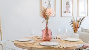 A round dining table with plates, glasses, and a pink vase with dried flowers. There are framed pictures on the wall behind the table. - Penthouse With Terrace and sea Views (Casares)