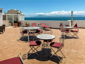 A terrace with outdoor seating, a view of the sea, and a building in the background. - Belvilla by OYO Apartamento PB 1 Dormitorio 1-6 (Tarifa)