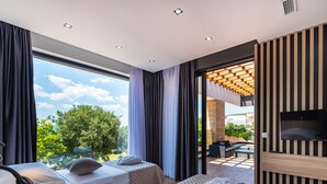 Quarto de hotel moderno com duas camas, televisão e varanda com vista para a cidade.