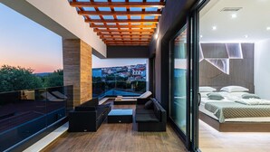 Uma varanda moderna com pérgola de madeira, guarda-corpo de vidro e área de estar com almofadas.