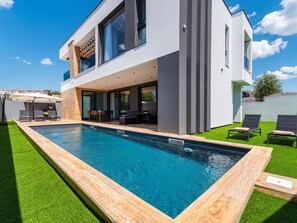 Una moderna casa a due piani con piscina, area salotto esterna e prato curato.
