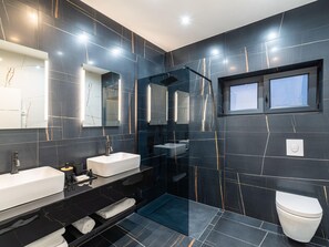 Un bagno moderno con piastrelle in marmo scuro, box doccia in vetro, lavandino bianco e water.