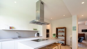 Una cocina moderna con armarios blancos, una isla central con taburetes, una campana extractora de acero inoxidable y un horno empotrado.