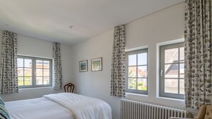 Un dormitorio con cama, dos ventanas, un radiador y una silla.