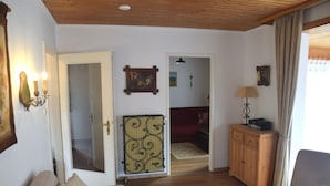 A living room with a beige sofa, a wooden cabinet, a lamp, and a door leading to another room. - Garden Apartment in Fussen (Fuessen)