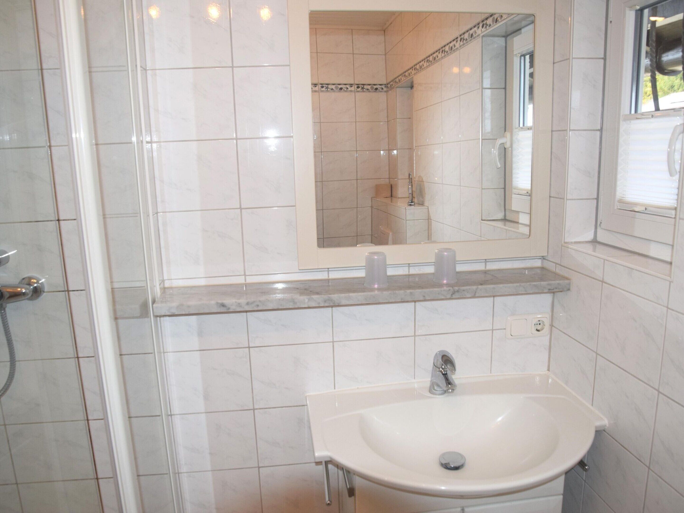 A bathroom with a sink, mirror, and shower.