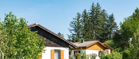 A row of wooden cabins with white walls and brown roofs, surrounded by lush greenery and tall trees.