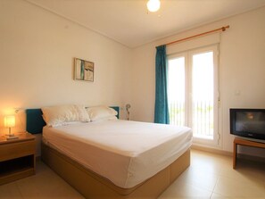 A bedroom with a bed, a nightstand, a lamp, a TV, a painting on the wall, and a window with curtains. - Penthouse in Sucina With Pool and Golf (Murcia)