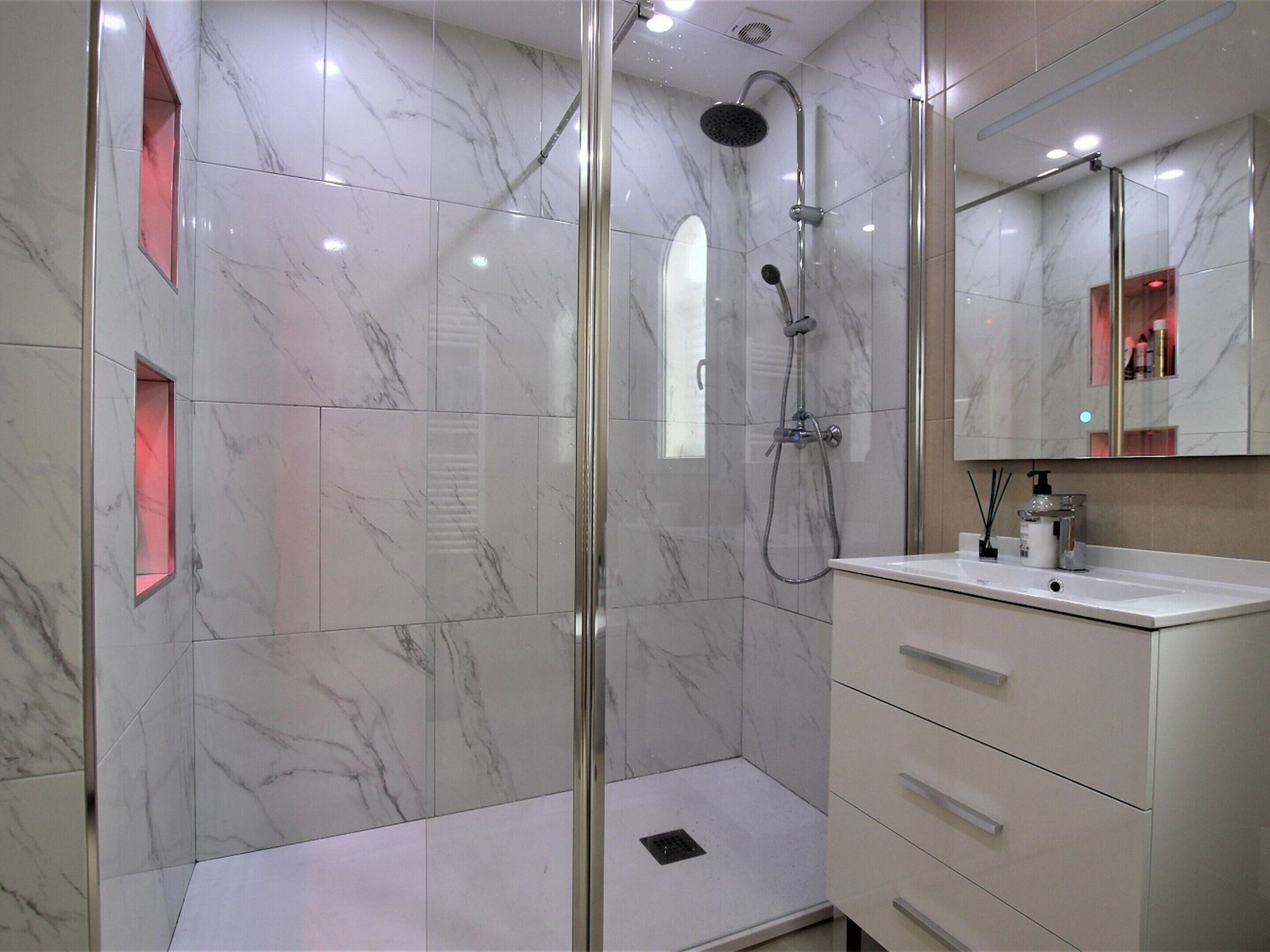 Un bagno moderno con cabina doccia in vetro, pareti in marmo e un mobile vanitario con cassetti.