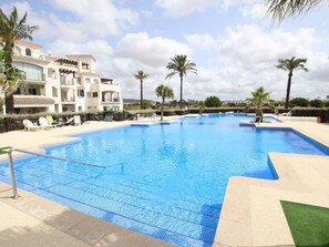 A swimming pool with a tiled deck, surrounded by palm trees and a building with balconies. - Penthouse in Sucina With Pool and Golf (Murcia)