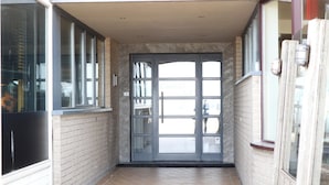 Un couloir étroit avec une porte en verre donnant sur une pièce. Le couloir est doté d’un sol carrelé et de murs en briques.