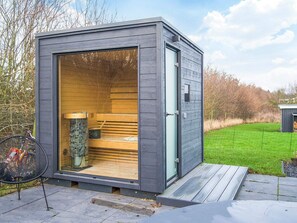 Een moderne, compacte sauna met een glazen deur, houten banken en een metalen stoel erbuiten.