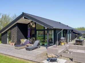 Een modern huis met een houten terras, buitenmeubels en een vuurkorf.