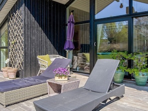 A covered outdoor seating area with wicker lounge chairs and a small table with flowers. - 5 Star Holiday Home in Horve (Follenslev)