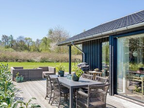 A deck with outdoor furniture, a grill, and a glass door leading to a garden.