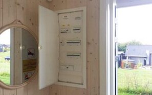 Une pièce avec un mur en bois, un miroir rond et un panneau électrique blanc doté de plusieurs interrupteurs et indicateurs.