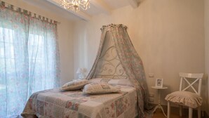 Un dormitorio con cama con dosel, candelabro, mesita de noche pequeña con lámpara y una silla.