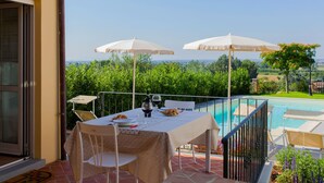 Una terraza con una mesa lista para dos, con vistas a una piscina y abundante follaje.