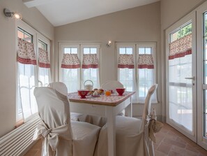 Comedor con una mesa dispuesta para cuatro personas, sillas blancas y una ventana con cortinas.