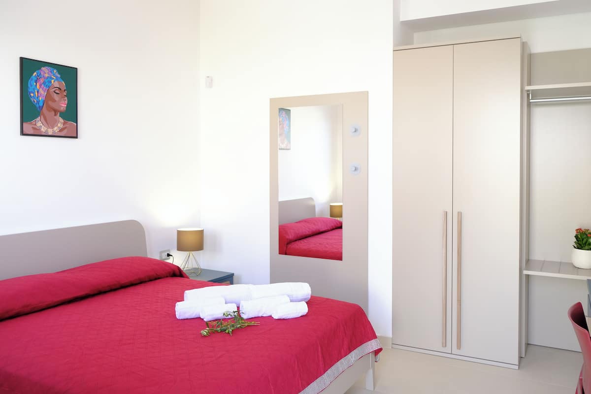 Ein Hotelzimmer mit Bett, Spiegel, Kleiderschrank und einem kleinen Tisch mit Lampe.