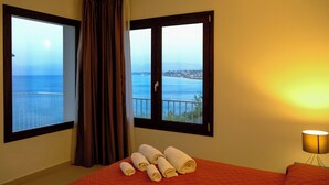A hotel room with a bed, a window with curtains, a lamp, and a view of the sea. - Sol Y Mar Camere e Appartamenti (Castellammare del Golfo)