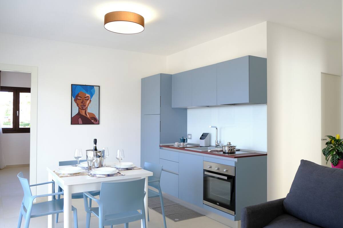 Eine moderne Küche mit blauen Schränken, einer Holzauskładung und einem eingebauten Ofen. Es gibt einen Esstisch mit Stühlen und ein Bild an der Wand.