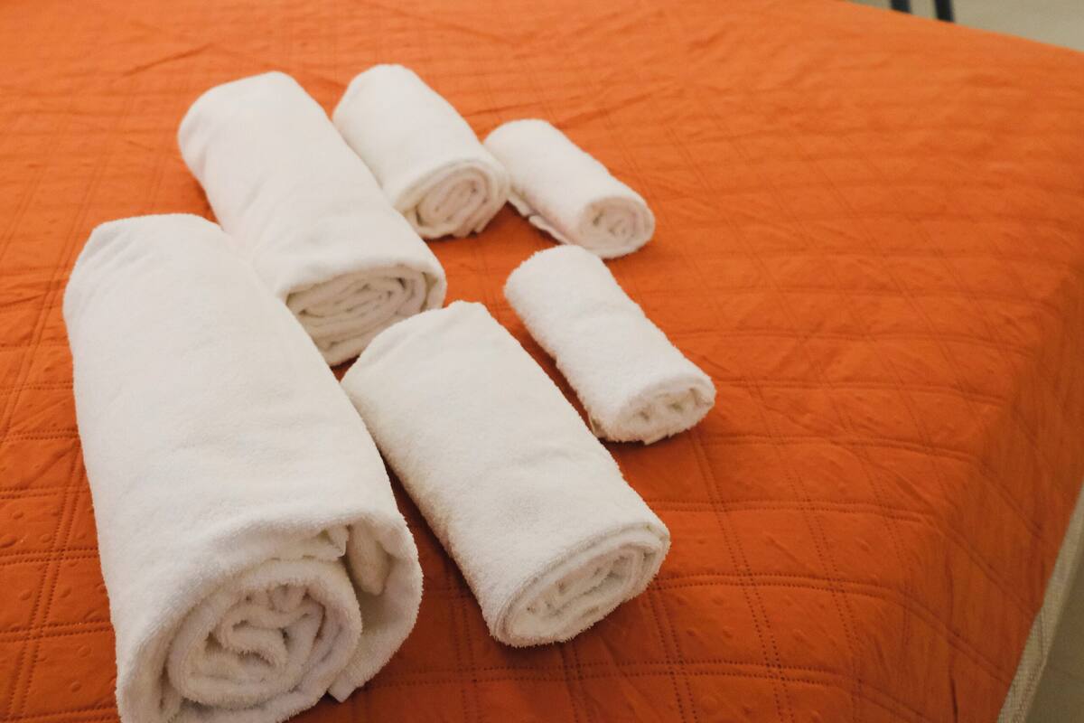Ein Hotelzimmer mit orangefarbener Bettdecke, einem Etagenbett und gerollten weißen Handtüchern auf dem Bett.