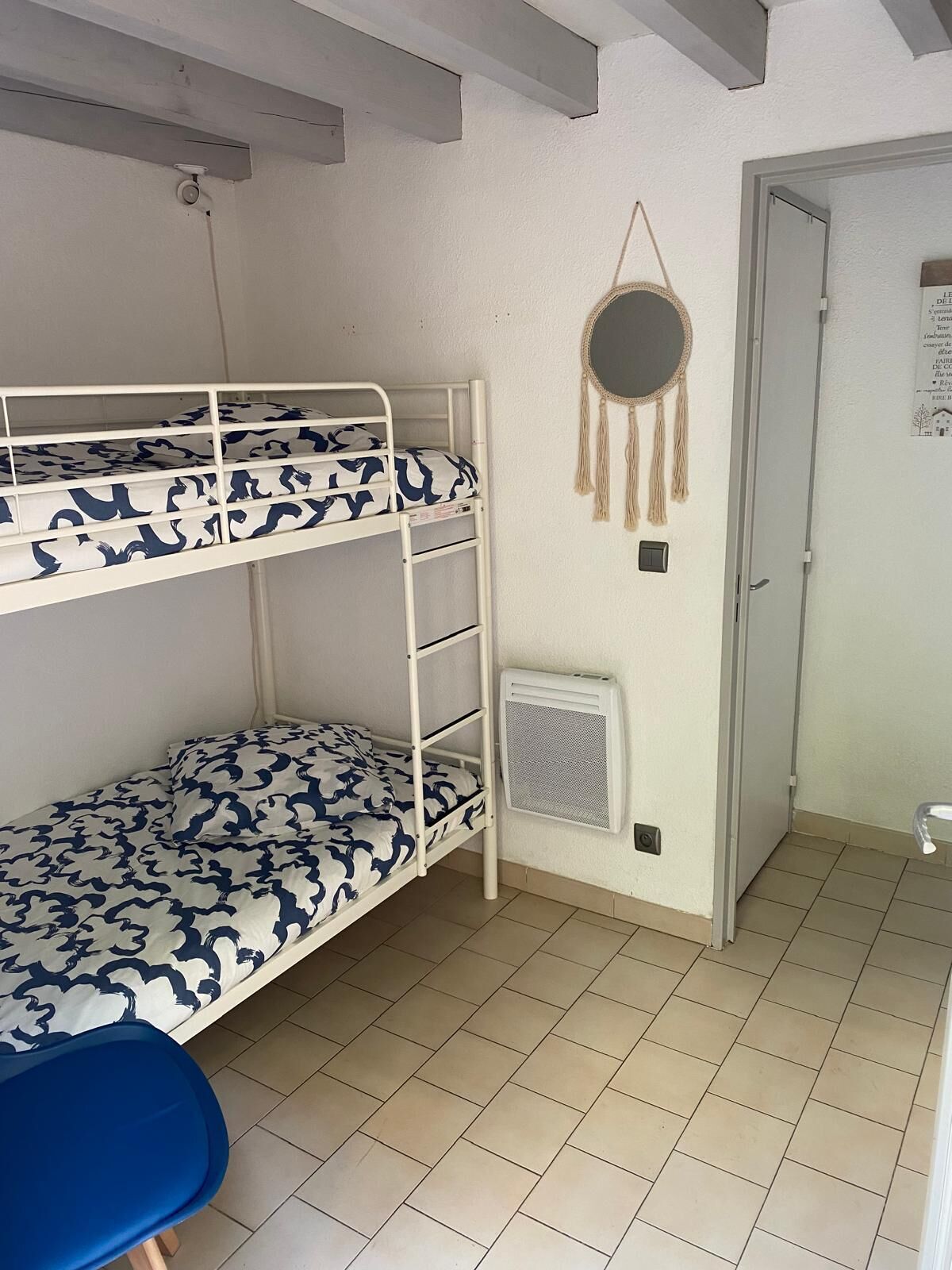 A bunk bed room with a patterned bedspread, a round wall hanging, and a door with a poster.