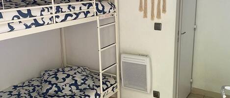 A bunk bed room with a patterned bedspread, a round wall hanging, and a door with a poster.