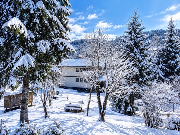 Un paisaje nevado con una casa, árboles y un banco.