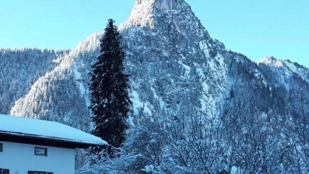 Una casa con techo nevado y una montaña al fondo.