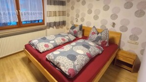 Un dormitorio con dos camas individuales, cabecera de madera, una mesita de noche de madera, un radiador y una ventana con cortinas.