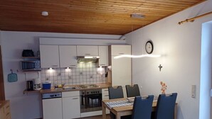Cocina compacta con armarios blancos, microondas, estufa y comedor con mesa y sillas.
