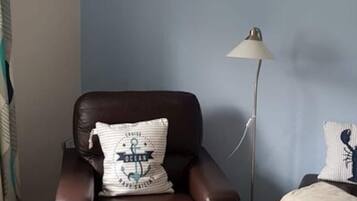 A brown leather armchair with a nautical-themed pillow, a floor lamp, and a small table with a basket of items.