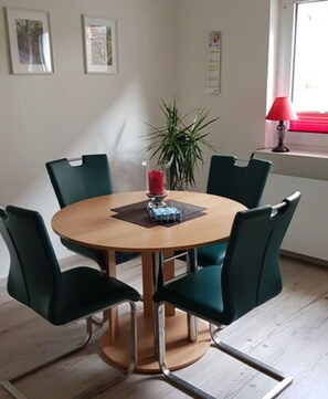 A round wooden table with four green chairs, a red candle, and a small blue box on a placemat. - Lovely Apartment in Hesse (Berkatal)