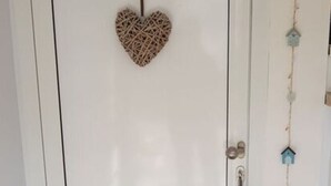 Una puerta blanca con una decoración con forma de corazón colgada encima y una guirnalda de adornos con forma de casa de pájaros al lado derecho.