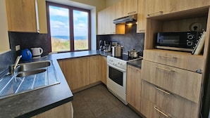A compact kitchen with wooden cabinets, a stove, a microwave, and a large window offering a view. - Well-equipped Holiday Home With Terrace (Stavelot)