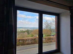 A room with a large window offering a view of a road, trees, and distant hills. - Well-equipped Holiday Home With Terrace (Stavelot)