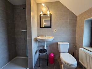A bathroom with a shower, sink, toilet, and a small stool.