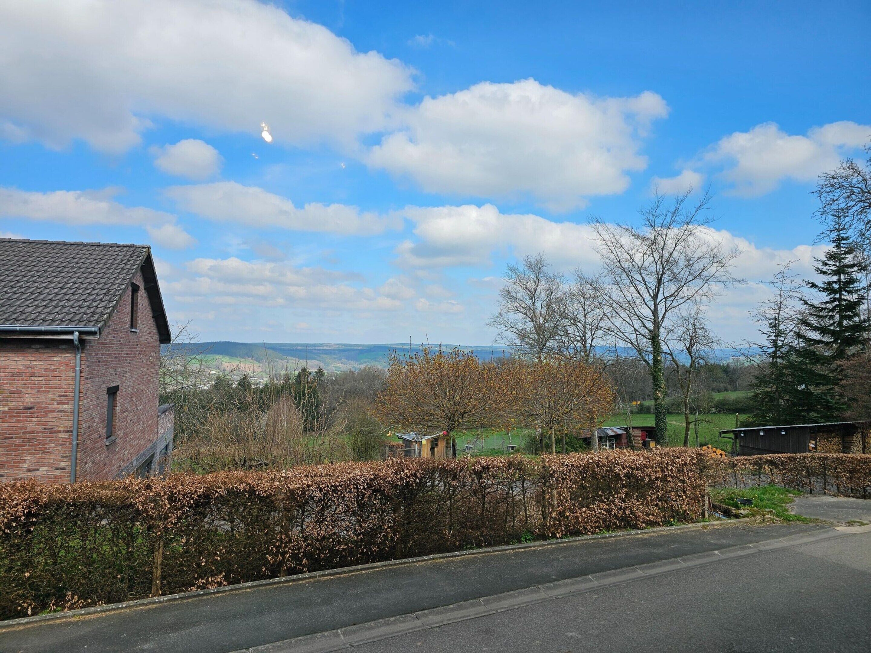 A rural landscape with a brick building, a road, and a hedge.
