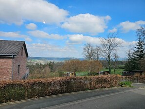 A rural landscape with a brick building, a road, and a hedge.
