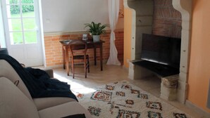 Un salon comprenant un canapé, un téléviseur, une cheminée, une table à manger avec des chaises et une plante en pot.