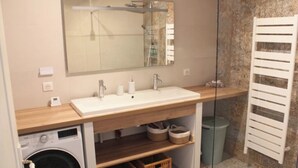 Une salle de bain avec un meuble-lavabo en bois, un grand miroir, un lave-linge et un porte-serviettes.